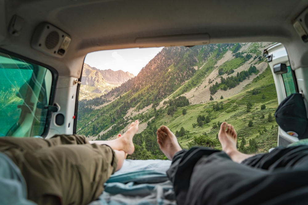 Výhľad na horskú krajinu z otvoreného kufra auta, dvaja relaxujú a užívajú si prírodu.