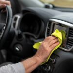 Vodič utiera vlhkosť z palubnej dosky auta žltou handričkou.