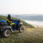 Štvorkolka zaparkovaná pri horskej chate, s pohľadom na les a kopce v pozadí.